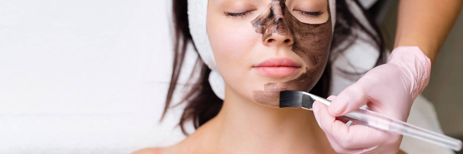 cosmetologist applying black mask pretty woman face wearing black gloves gorgeous woman spa having facial procedures 1